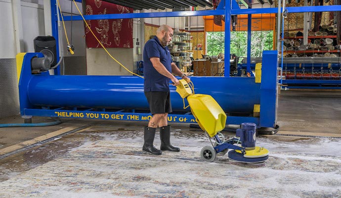 A professional rug cleaner using a scrubber machine to deep clean a soapy area rug