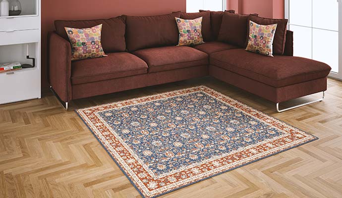 Square blue and terracotta patterned area rug placed before a sectional sofa