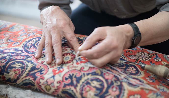 Craftsman hand stitching and repairing damaged fibers on an oriental area rug
