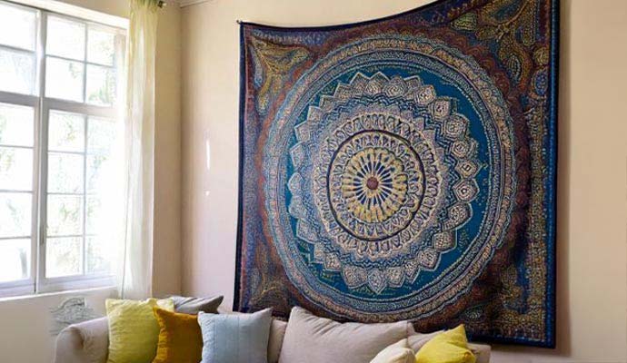 Large decorative tapestry with circular mandala design hanging on a wall above a couch
