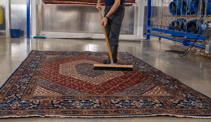 A professional rug cleaner using a long-handled brush to scrub a large oriental rug in a cleaning facility