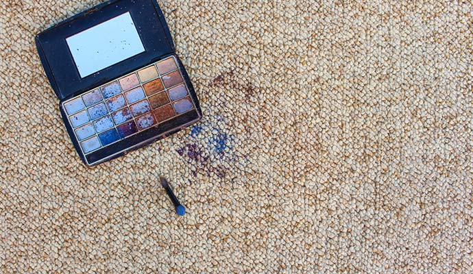 Broken makeup powder palette spilling eyeshadow stains onto carpet fibers