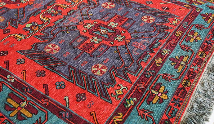 A close-up view of an oriental rug featuring intricate geometric patterns in red, purple, and teal
