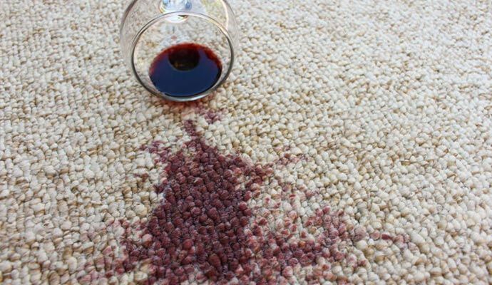 Spilled glass of red wine creating a large visible stain on a beige carpet