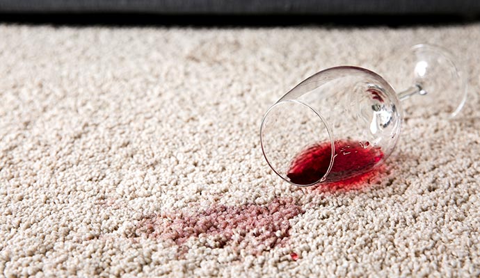 A wine glass spilled onto a rug, leaving a visible red stain on the rug