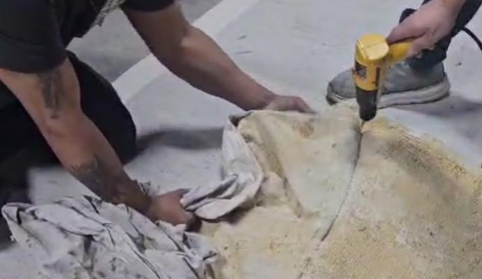 Technician removing damaged rug backing using tools to restore support and stability