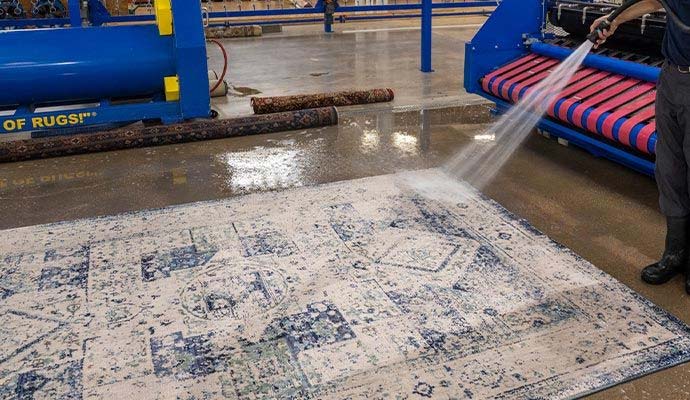 Technician spraying and rinsing an area rug during wet cleaning